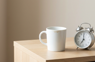 A white coffee cup and a classic alarm clock on a wooden table, representing morning fatigue and excessive yawning causes.