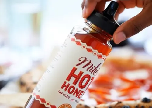 Bottle of Mike’s Hot Honey held over food — article explores its health benefits, risks, and safe use.