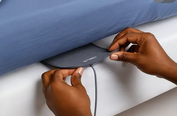 Withings Sleep Analyzer being placed under a mattress to track sleep, heart rate, and breathing patterns.